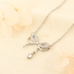 Elegant 925 silver bow necklace with sparkling zircon pendant on soft beige background