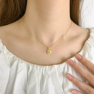 Collier élégant en or avec pendentif carré en cristal jaune porté sur le cou d'un mannequin