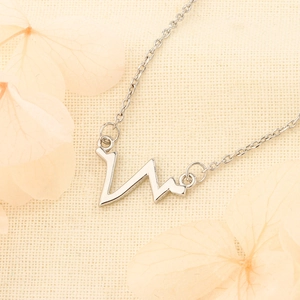 Minimalist heartbeat pendant necklace in silver stainless steel on textured fabric