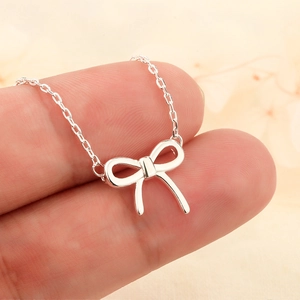 Silver bow pendant necklace with fine chain link held between fingers for detail