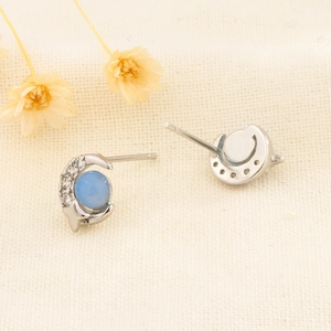 Boucles d'oreilles lune et étoile en argent avec opale bleu clair sur tissu beige