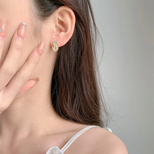 Close-up of a sparkling gold dollar sign stud earring with pavé crystals on a female model