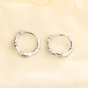 Macro detail of silver bamboo joint hoop earrings on a textured linen background