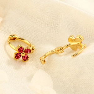 Boucles d'oreilles trèfle dorées avec zircons rouges sur fond en tissu beige