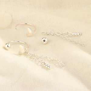 Detail of silver heart tassel earrings with delicate chains on a beige fabric background