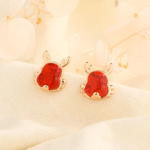 Detail of red cartoon dragon stud earrings with gold accents on creamy fabric background