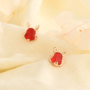 Macro detail of red festive reindeer stud earrings with golden antlers on textured fabric