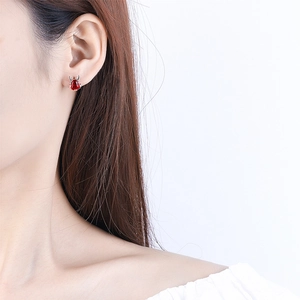 Close-up of red gemstone lucky bag stud earring worn by model in pure white setting