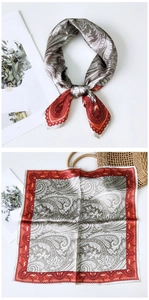 Détail d'un foulard en soie à motif paisley gris et rouge, noué et posé à plat