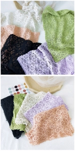 Detail of delicate floral hollow lace shawl with fringe balls in multiple pastel colors