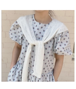 Detail eines weißen Strickschals über einem blauen Blumenkleid mit Puffärmeln
