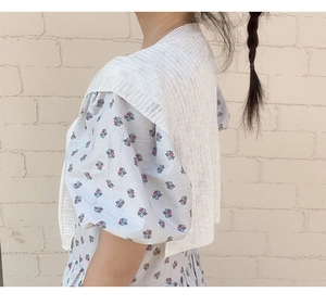 Detail der cremefarbenen Strickweste über hellblauem Sommerkleid mit Puffärmeln