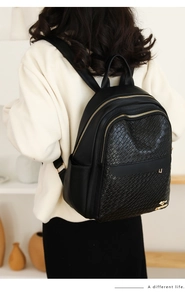 Detail of black leather backpack featuring woven texture, gold kangaroo logo and zippers