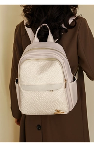 Detail of cream-colored woven leather backpack featuring a golden kangaroo logo and zipper