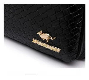 Detail of black faux crocodile leather texture and golden kangaroo metal logo on the bag