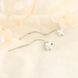Macro detail of silver four-leaf clover earrings with zircon inlay on linen background