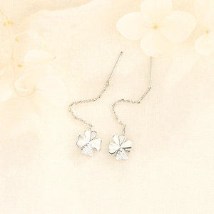 Close-up of silver four-leaf clover drop earrings with micro-set zircon on linen background