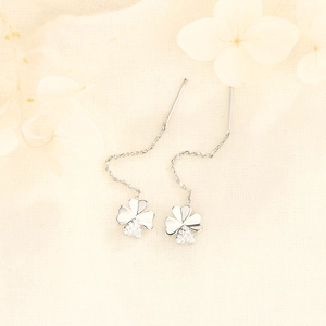 Silver four-leaf clover drop earrings with crystal pavé on light beige fabric