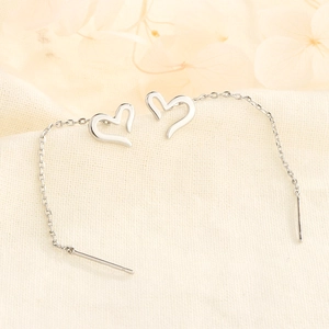 Elegant heart-shaped drop earrings with delicate silver chains on a minimalist textured background
