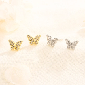 Détail de boucles d'oreilles papillon dorées et argentées serties de zircons cubiques