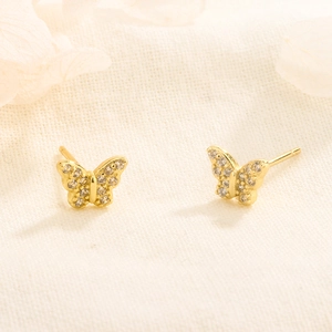 Vue macro des boucles d'oreilles papillon dorées avec zircons sertis sur tissu en lin