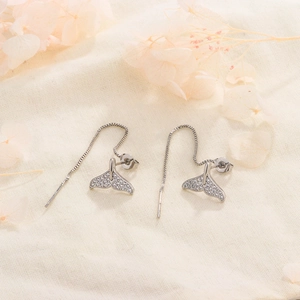 Elegant silver fish tail drop earrings with cubic zirconia fringe on beige linen background