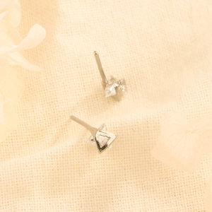 Minimalist silver triangle stud earrings with clear zircon on textured linen background
