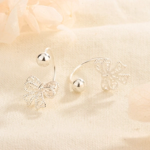 Silver hollow lace bow stud earrings with vintage screw back design on beige fabric