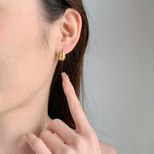 Close-up of elegant gold water drop hoop earrings worn by a model in a minimalist style