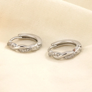 Boucles d'oreilles créoles Mobius argentées avec cristaux de zircone sur fond beige