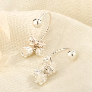Vue détaillée des boucles d'oreilles muguet avec nœud en argent sur tissu en lin