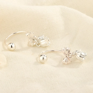 Détail de boucles d'oreilles nœud argenté avec pampilles muguet sur fond de lin