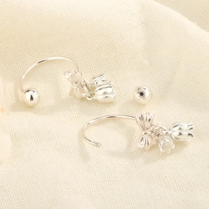Détail de boucles d'oreilles nœud et muguet en argent sur fond en lin beige