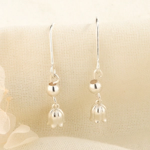Macro shot of silver lily of the valley earrings on a textured beige fabric background