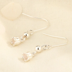 Macro shot of silver lily of the valley drop earrings on a textured fabric background