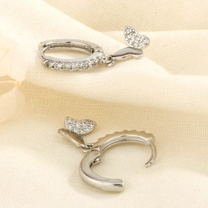 Élégantes boucles d'oreilles papillon en argent avec zircons sur fond de tissu beige