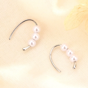 Detail of silver drop hook earrings featuring three elegant white pearls on fabric