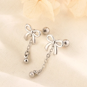 Detail of silver bow tassel earrings with fine chain and screw ball back on linen cloth
