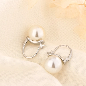 Close-up of elegant pearl drop earrings with silver clasps on beige knit fabric