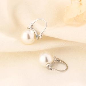 Detailed close-up of round pearl earrings with silver leverback clasp on linen fabric