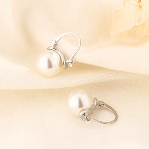 Elegant vintage pearl drop earrings with silver hooks on minimalist beige fabric background