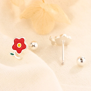 Vue détaillée de boucles d'oreilles fleur rouge à vis sur tissu beige texturé
