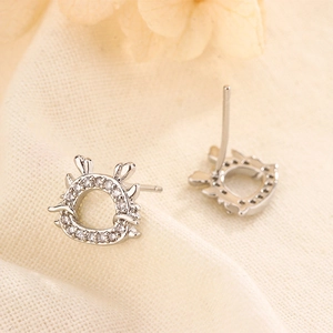 Detailed close-up of dragon stud earrings with clear crystals on a beige fabric background
