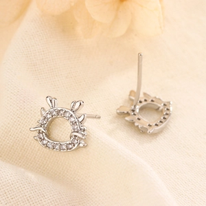 Silver dragon stud earrings with sparkling white zircons on soft textured fabric