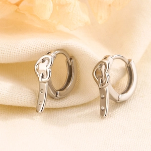 Macro view of silver heart-shaped belt buckle earrings on elegant textured fabric