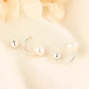 Macro shot of C-shaped freshwater pearl earrings with screw ball back on linen
