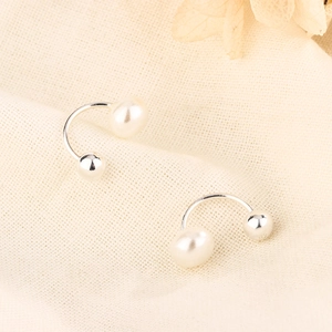 Macro shot of U-shaped freshwater pearl earrings on soft fabric with dried flowers