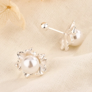 Macro shot of silver flower pearl earrings on a soft linen fabric with dried petals