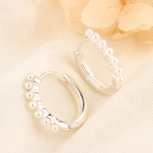 Macro shot of silver pearl hoop earrings with refined beads on beige linen cloth