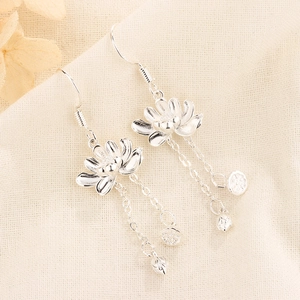 Détail des boucles d'oreilles lotus avec de longs glands sur tissu en lin naturel